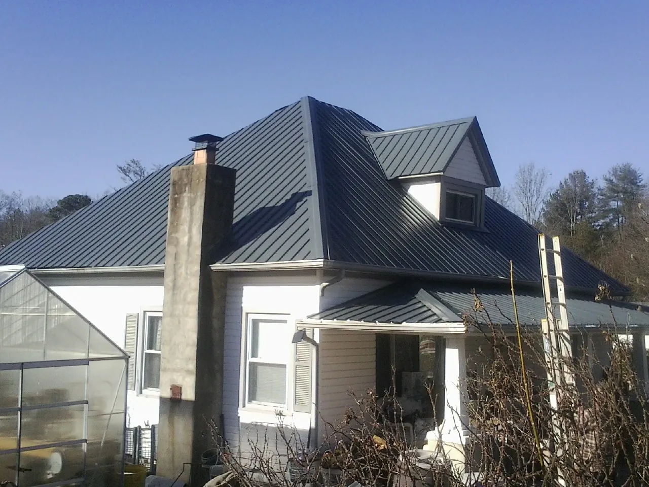 Dark blue standing seam metal roof on a white farmhouse with dormer — Slate & Tile Roof Repair by Roofing Brothers in Vanceboro