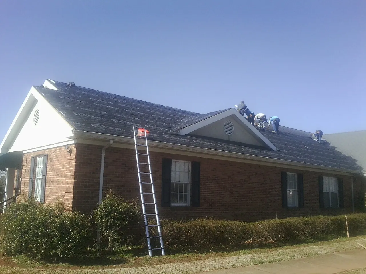 Crew tearing shingles off a brick ranch roof with a ladder set — Metal Roof Repair work by our crew in Vanceboro