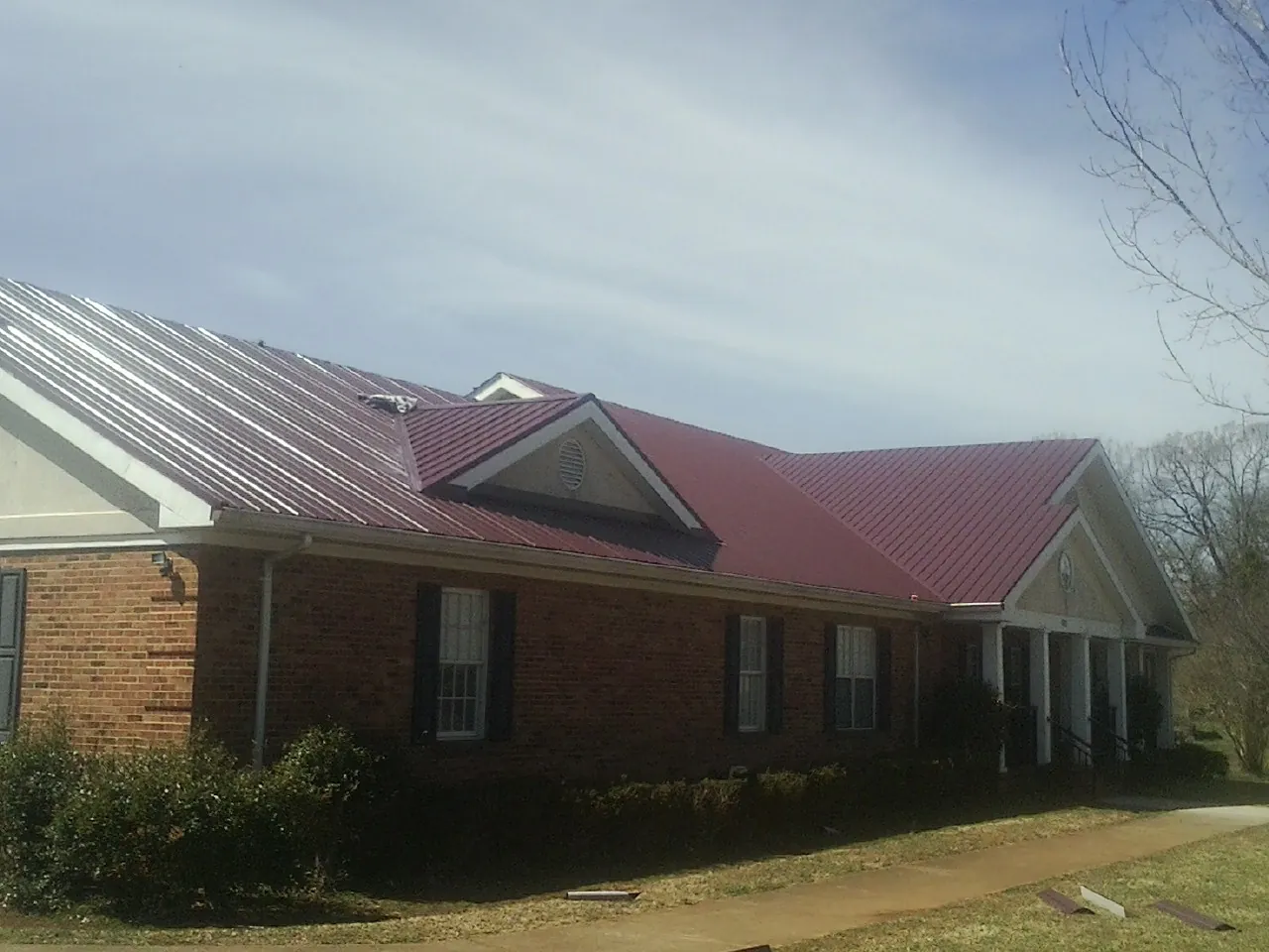 Red metal roof with gabled entries on a long brick building, from a Hail Damage Roof Repair job in Vanceboro