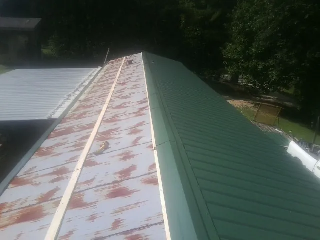 Old rusted panels beside newly installed green metal roofing — Wind Damage Roof Repair by Roofing Brothers in Vanceboro