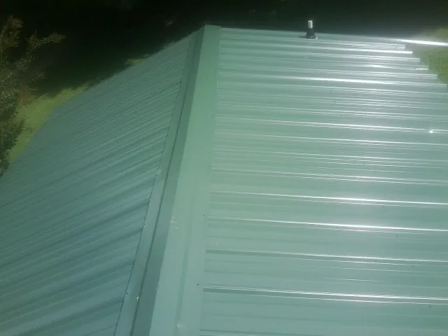 New green metal panels meeting at the ridge of a roof — Flat Roof Repair work by our crew in Vanceboro