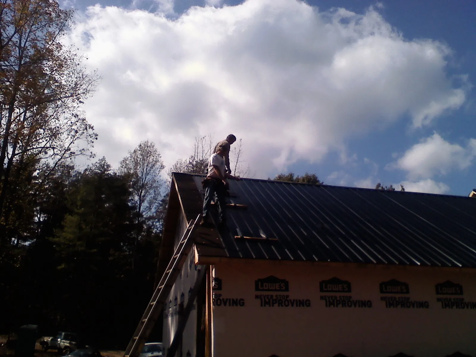 Roofer fastening dark metal panels high against a cloudy sky, from a Roof Inspection job in Vanceboro