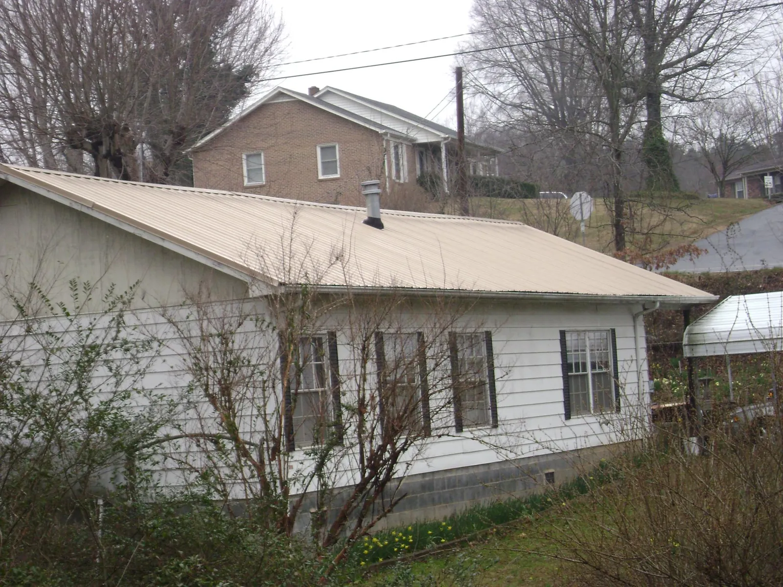 Tan metal roof on a white sided house set into a hillside — Commercial Roofing by Roofing Brothers in Vanceboro