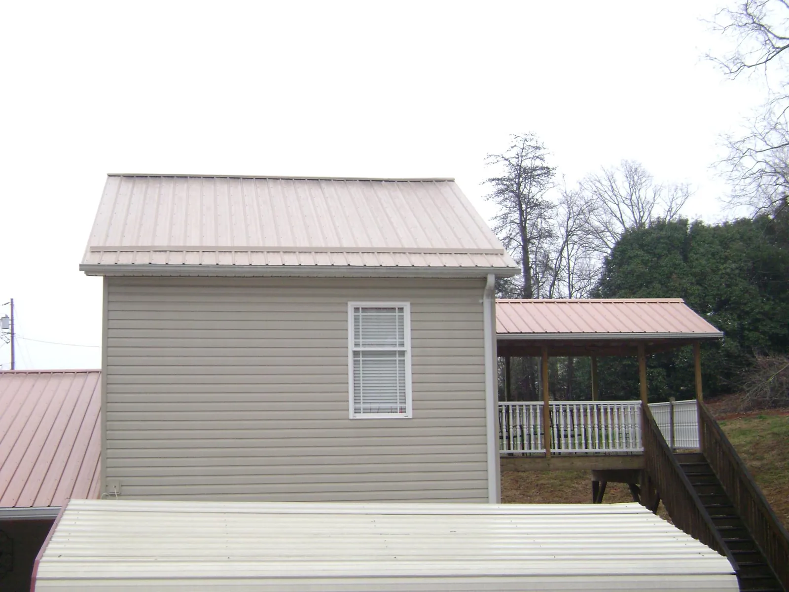 Tan metal roofs on a two story addition and attached porch, from a Roof Replacement job in Vanceboro
