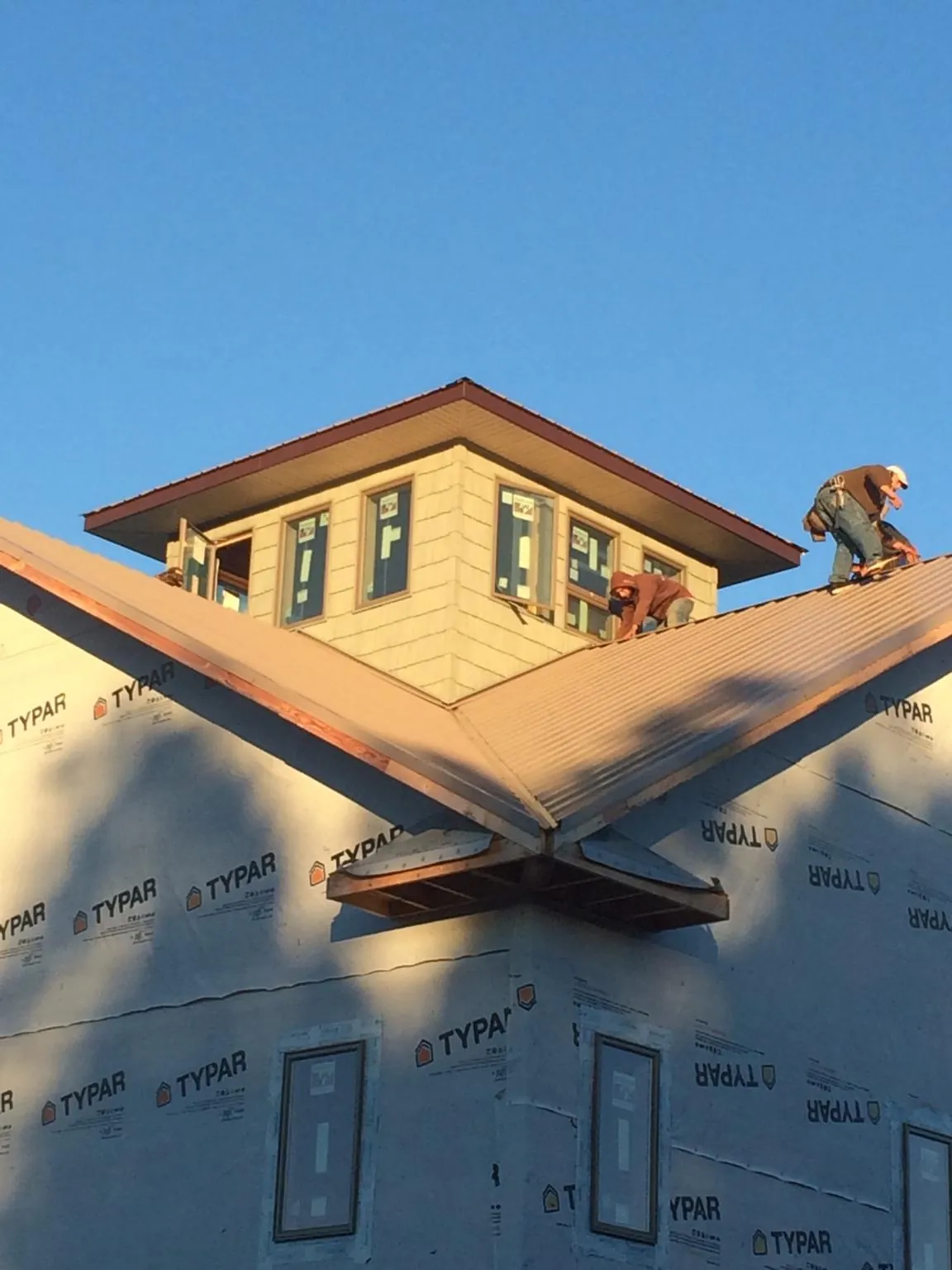 Roofers working around a rooftop cupola on a new metal roof at sunset in Vanceboro